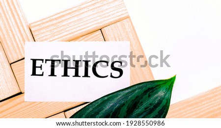 On a white background wooden building blocks, a white card with the text ETHICS and a green leaf of the plant. Template. View from above