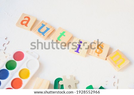 watercolor paints and children's educational toys on a light background, the inscription autism on wooden squares, treatment and diagnosis of autism concept