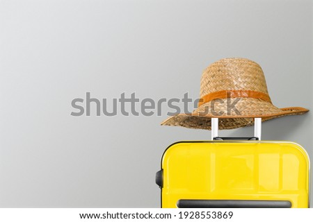 Bright and stylish yellow suitcase with straw hat against a trendy gray background.