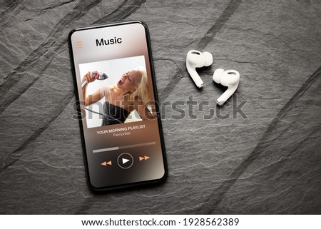 Music player on screen of mobile phone and wireless earphones on dark background