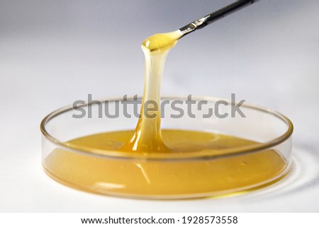 A viscous yellow liquid such as glue or honey isolated on a white background. The liquid is in a round container, taken with a stick with a spoon and its yellow transparent color and viscosity are sho Royalty-Free Stock Photo #1928573558