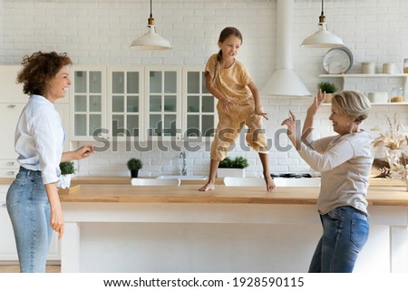 Active family of 3 female generations retired grandma adult mom little daughter grandchild have fun dance at modern kitchen. Energetic dynasty granny mom kid girl jump by music on funny party at home Royalty-Free Stock Photo #1928590115