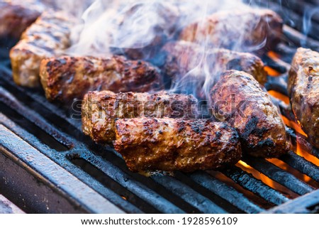 Preparing meat rolls called mici or mititei on barbecue. close up of grill with burning fire with flame and smoke. Royalty-Free Stock Photo #1928596109