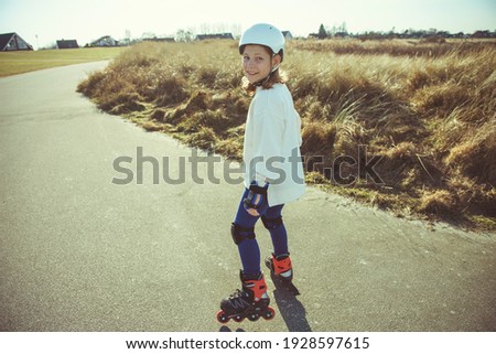 Happy teenager child girl in white helmet, inline skates and safety equipment having fun during learning skating at sunny day