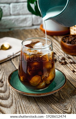  Cream is poured into a glass of iced coffee, vertical photo. High quality photo