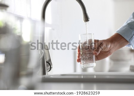 Man pouring water into glass in kitchen, closeup Royalty-Free Stock Photo #1928623259