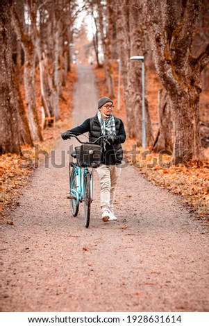Man walking alone on a path with his bike during autumn next to many trees