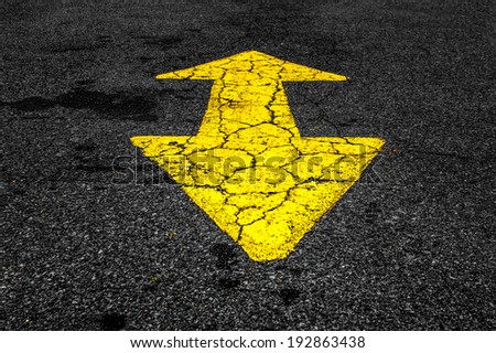 Yellow traffic directional arrow on cracked asphalt road