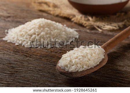 Raw white rice in a ceramic bowl on brown wooden background.