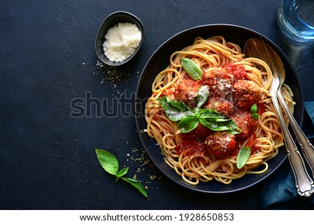 Spaghetti with meat balls in tomato sauce in a black bowl on a dark slate, stone or concrete background. Top view with copy space. Royalty-Free Stock Photo #1928650853