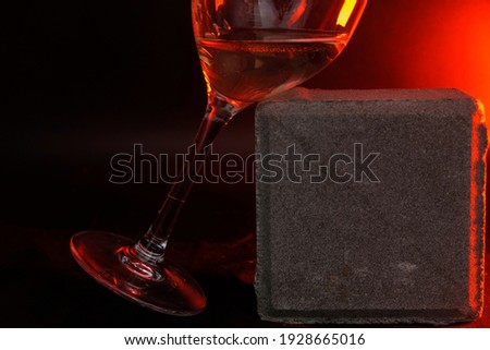 The leg of the wine glass. The glass is tilted. Blurred gray square stone background. Red light. Dark photo. Copy space.