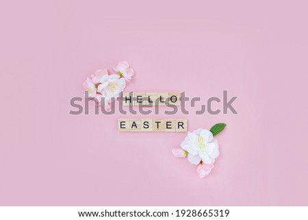 Phrase Hello Easter laid out from wooden letters on pink background and decorated with spring flowers. Flat lay, top view
