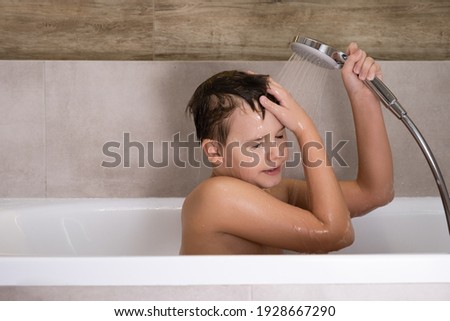 The boy holding shower head and washes his head in bathroom Happy healthy childhood Royalty-Free Stock Photo #1928667290