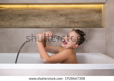 Happy boy holding shower head and singing while washing in bathroom Child bathe at home healthy childhood Royalty-Free Stock Photo #1928667308