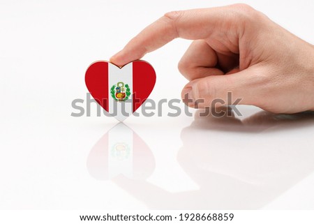 Peru flag. Love and respect Peru. A man's hand holds a heart in the shape of the Peru flag on a white glass surface. The concept of Peruvian patriotism and pride.