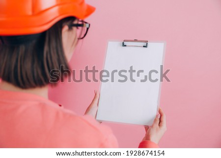Woman worker builder hold white sign board blank against pink background. Building helmet. Back to camera.