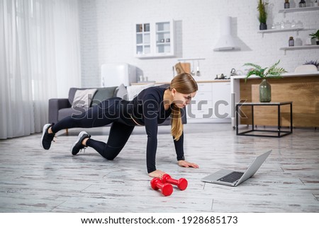 Young slender woman goes in for sports at home. A beautiful sportswoman with blond hair is doing exercises, watching an online workout on a laptop at home. Fitness at home during quarantine.