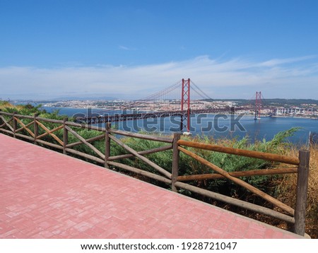 Ponte 25 de Abril Bridge. Red, Golden Gate-style, beautiful suspension bridge links Lisbon with Almada. Panoramic view from Christ the King Square. Observation deck with pink tiles and wooden fence.
