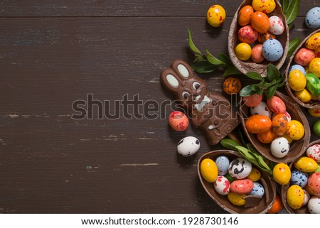 Easter hunt concept background with chocolate eggs and bunny on wooden table copy space. View from above