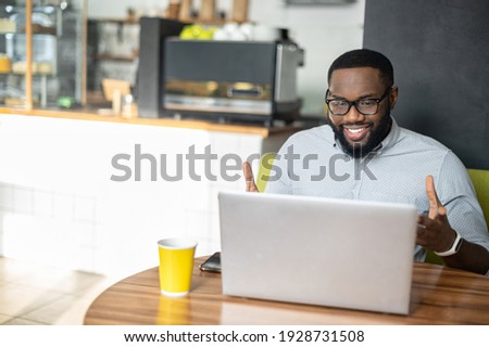 Smiling African-American guy is using a laptop for video call sitting in the cozy cafe. A multiracial young man talks online, has video meeting working remotely