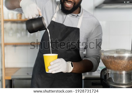 Close-up biracial barista preparing latte coffee to go, a multiracial waiter pouring milk into paper cup, take-away hot drinks order, cropped picture