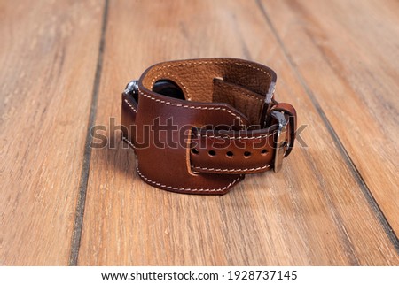 Dark brown leather strap attached to the smart watch on a wooden floor.