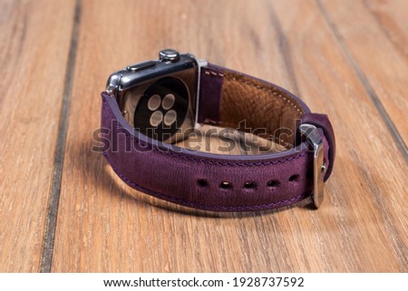 Purple leather strap attached to the smart watch on a wooden floor.