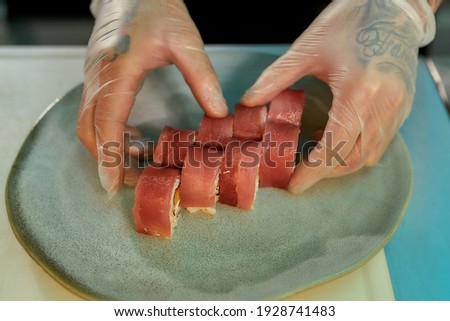 Closeup of hands of chef placing sliced tuna sushi on a plate while preparing rolls at commercial kitchen. Food photography, Japanese cuisine, restaurant service concept