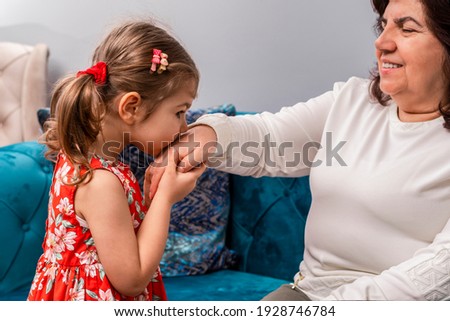 Little baby girl kiss her grandmother's hand during Eid mubarak (Turkish Ramazan or Seker Bayram). Adorable child kiss elderly woman hand to show respect. Cute toddler follow muslim Ramadan traditions