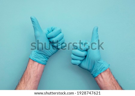 Doctors hand wearing protective surgical gloves giving thumbs up sign.