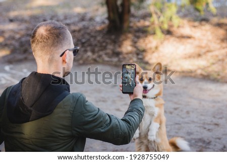 youg man taking a photo of his welsh corgi pembroke dog