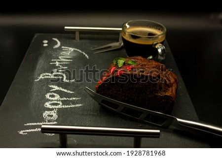 Darck food happy birthday writing chalk chocolate pancake garnished with mint and red glass with coffee to accompany