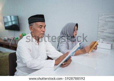 Asian Muslim senior man teaching wife reading Koran or Quran in living room. muslim couple praying at home