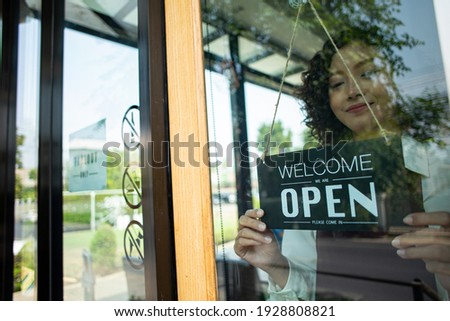 Store owner woman turning open sign wood broad to ready service food and beverage to customer.Asian entrepreneur leaning.Asian waiter stand and flip advertise hanging in front of coffee shop.