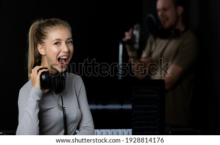 Portrait of a young and beautiful female singer with microphone and equipment working in voice recording studio. She poses to camera with happy, cheerful and cheerful.