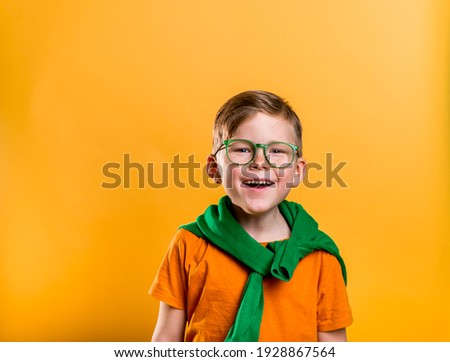 Happy ginger boy with freckles on Saint Patrick Day. Kid in green glasses and orange t-shirt. Patrick party with Irish culture and traditions. Bright child boy with leprechaun for a St. Patrick's Day