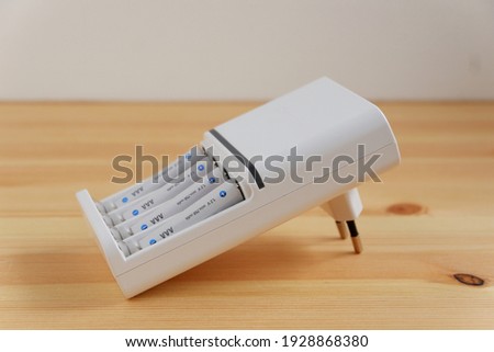 Rechargeable AAA battery in a white charger on wooden background. Royalty-Free Stock Photo #1928868380