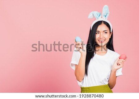 Happy Easter concept. Beautiful young woman smiling wearing rabbit ears holding colorful Easter eggs gift on hands, Portrait female looking at side away, studio shot isolated on pink background