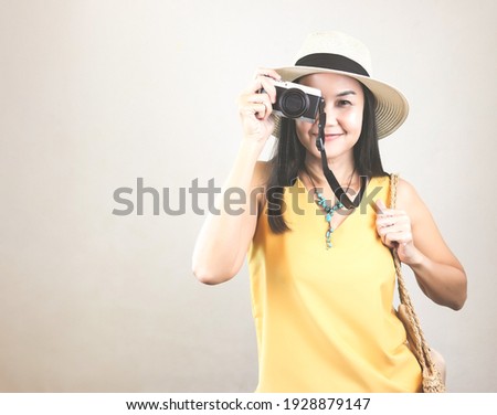 Portrait of asian female tourist wearing yellow sleeveless shirt and hat, covering eyes with camera smiling and looking at camera.