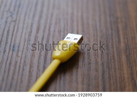 Yellow colored USB type cable staying on dark wooden table.