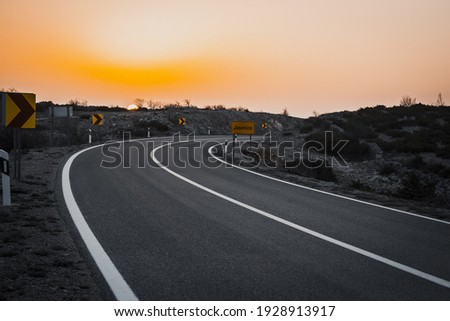 A view of an asphalt road with sunset scenery in the background Royalty-Free Stock Photo #1928913917