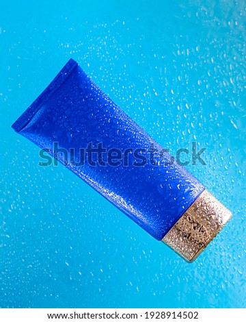 Cream cosmetic tube of blue color with a gold cap in clean transparent water with sunlight on a blue background. Natural organic cosmetology in a clean beautiful drop of water. Copy space