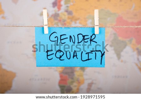 Gender Equality word written on a Blue color sticky note hanging with a wire in front of world map background