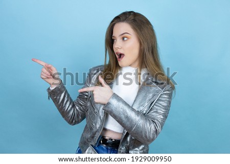 Pretty woman with long hair wearing a casual jacket over blue background surprised and pointing her fingers side