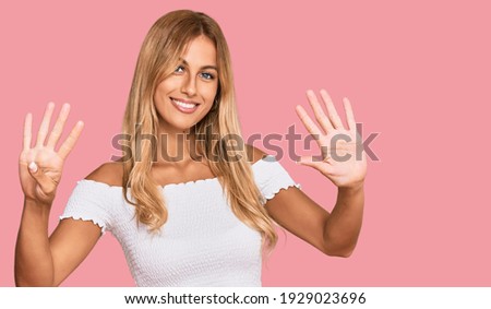 Beautiful blonde young woman wearing casual white tshirt showing and pointing up with fingers number nine while smiling confident and happy. 