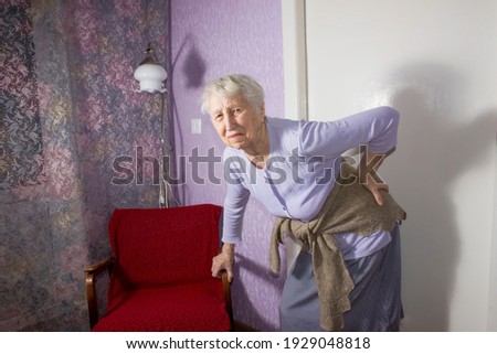 Elderly senior 75s woman with painful feelings massaging low back to reduce ache, backache discomfort. Diseases of older people, sciatic nerve injury concept Royalty-Free Stock Photo #1929048818