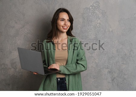 Happy beautiful brunette girl smiling while using laptop isolated over grey wall