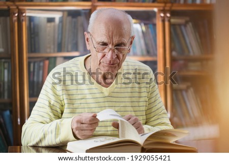 Mature professor wearing eyeglasses sitting at table and leaf through old book. Concept education and knowledge. Royalty-Free Stock Photo #1929055421