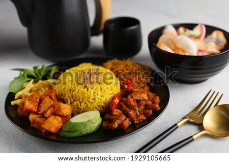 Nasi kuning or yellow rice is a traditional menu from indonesia. served with other dishes, such as fried chick, slices of omelette, cucumber, sambal goreng kentang and kering tempe on white background Royalty-Free Stock Photo #1929105665
