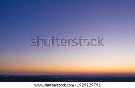 aerial of a deep blue sky with shining orange horizon and an aircraft flying through the frame  Royalty-Free Stock Photo #1929129791